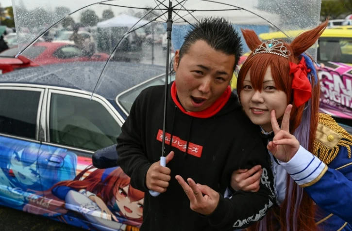 Yosuke Takahata (g) et une jeune femme en costume de l'héroïne d'animation Daïwa Scarlet devant une voiture personnalisée, pendant le festival "Itasha Tengoku", le 26 mars 2023 à Tokyo