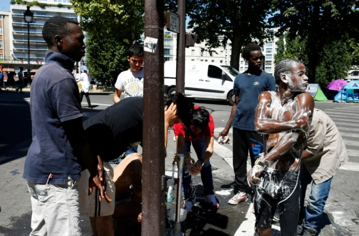 Les habitants d'un campement de migrants installé sous le métro aérien font leur toilette, le 19 juillet 2016 dans le nord-est de Paris