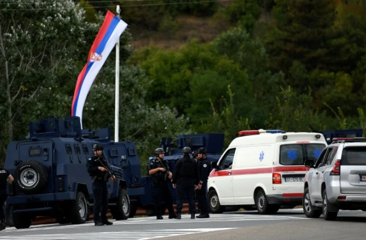 Des policiers kosovars montent la garde sous un drapeau serbe à l'entrée du village de Banjska, dans le nord du Kosovo, le 24 septembre 2023