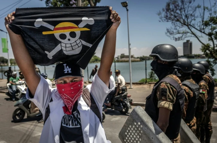 Un drapeau portant le logo du célèbre manga japonais One Piece, symbole adopté par les mouvements de protestation de la génération Z dans le monde entier, devant les forces de sécurité lors d'une manifestation exigeant de meilleures conditions de santé et des réformes constitutionnelles à Antananarivo, le 7 octobre 2025 à Madagascar