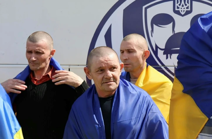 Photo diffusée par le Quartier général de coordination pour le traitement des prisonniers de guerre, le 19 août 2026, montrant d'anciens prisonniers de guerre ukrainiens, enveloppés dans des drapeaux nationaux, près d'un bus après un échange effectué dans un lieu tenu secret