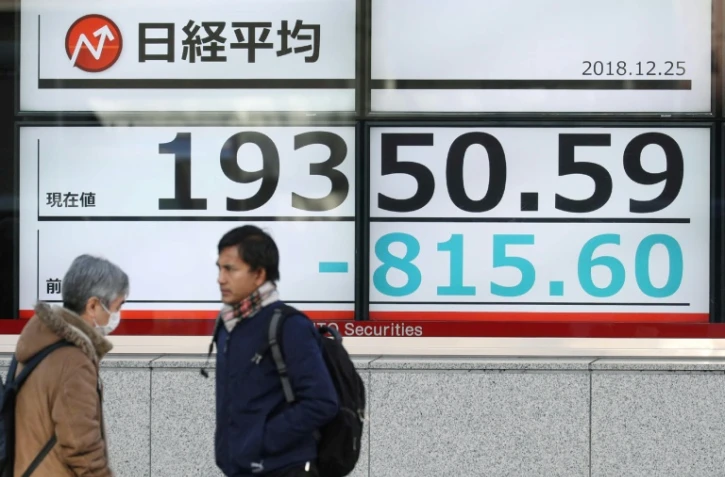 Des piétons passent devant un tableau d'indices boursniers, le 25 décembre 2018 à Tokyo, au Japon