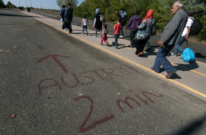 Des migrants passent près d'un message "Autriche-2 minutes", écrit au sol à la frontière austro-hongroise, près de Nickelsdorf, du côté autrichien, le 12 septembre 2015 