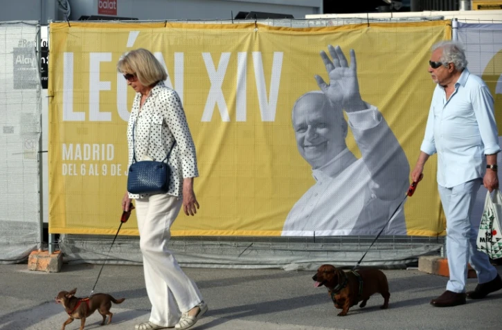 Deux personnes promènent leur chien près d'une affiche annonçant la venue du pape Léon XIV, le 5 juin 2026 à Madrid