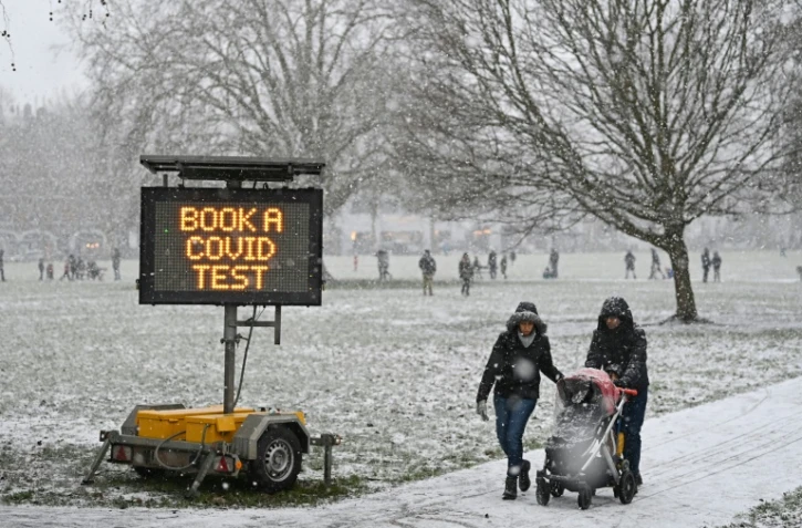 Des promeneurs passent près d'un panneau appelant à se faire tester au Covid-19, dans un parc de Londres sous la neige, le 24 janvier 2021