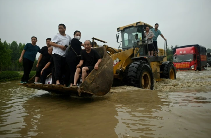 Des habitants évacués à bord d'un véhicule de chantier dans une rue inondée de la localité chinoise de Zhengzhou le 23 juillet 2021