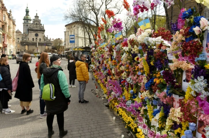 Des passants s'arrêtent devant un mur de fleurs artificielles et de photos de victimes tuées depuis le début de l'invasion russe, le 24 avril 2022 à Lviv, plus grand ville de l'ouest ukrainien