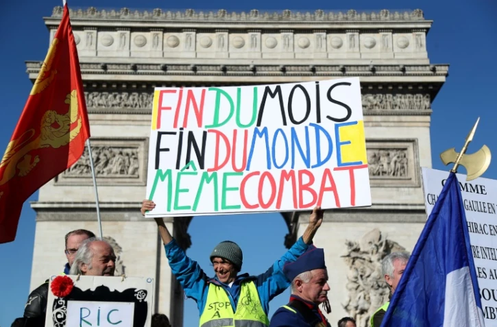 Le militant français Jean-Baptiste Redde, allias aka Voltuan (C) tient une banderole devant l'Arc de triomphe à Paris lors de l'acte 15 des Gilets Jaunes le 23 février 2019
