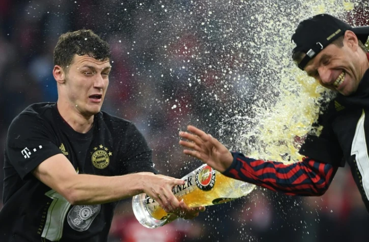 Le défenseur français du Bayern Munich Benjamin Pavard arrose de bière l'attaquant Thomas Mueller, après la victoire, 3-1 face au Borussia Dortmund, synonyme de 10e titre de champion consécutif, lors de la 31e journée de Bundesliga, le 23 avril 2022 à l'Allianz Arena