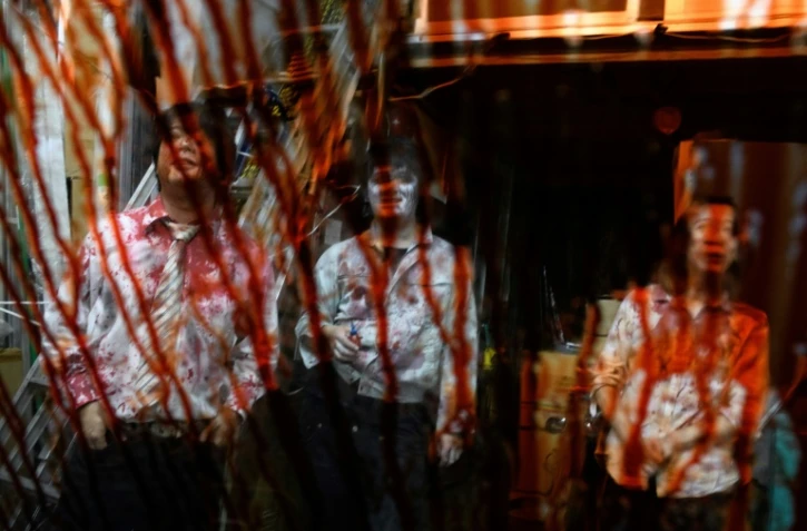 Les acteurs Kota Hanegawa (g), Kenta Iwana (c) et Asami Takeuchi, grimés en zombies, rôdent devant une voiture dont le pare-brise est couvert de faux sang, lors d'un spectacle de maison hantée en version drive-in, le 15 juin 2020 à Tokyo, au Japon
