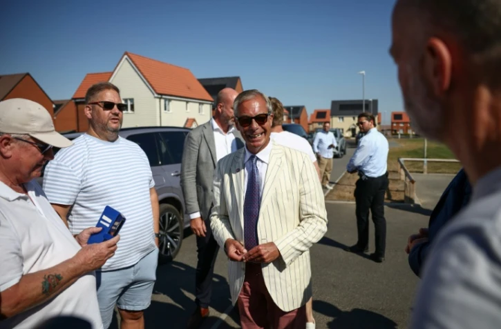 Nigel Farage, (c) chef du parti britannique Reform UK, parle avec des électeurs à la sortie d'un bureau de vote installé dans une école primaire de Walton-on-the-Naze, dans l'Essex, lors de l'élection partielle de Clacton, le 13 août 2026