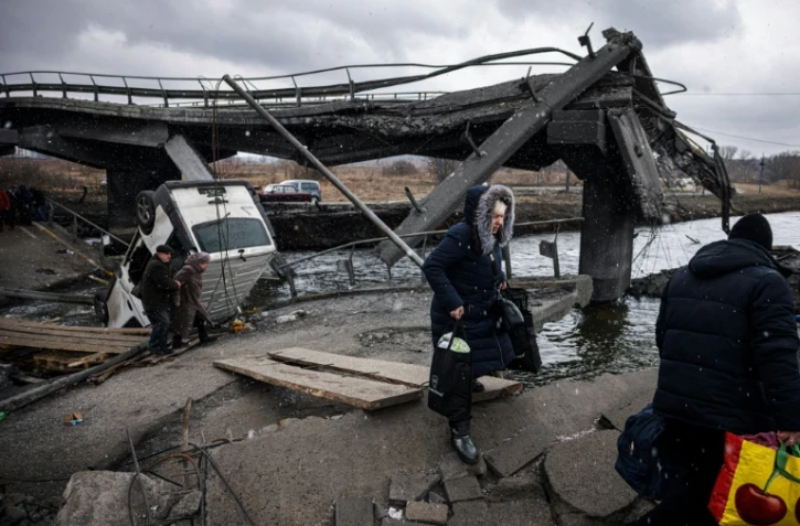 Des personnes fuient la ville d'Irpin, au nord-ouest de Kiev en traversant une rivière près d'un pont détruit, le 13 mars 2022