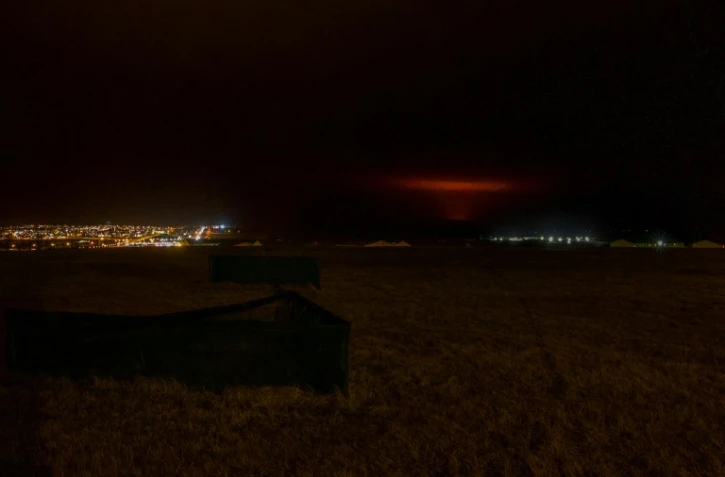 Un nuage rouge du magma lâché par le volcan Fagradalsfjall s'élève derrière la ville de Keflavik et l'aéroport international, à environ 50 km à l'ouest de la capitale de l'Islande, Reykjavik, le 19 mars 2021