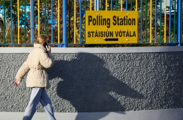 Une femme passe devant un panneau indiquant la direction d'un bureau de vote à Dublin le 25 novembre 2024, avant les élections législatives du 29 novembre