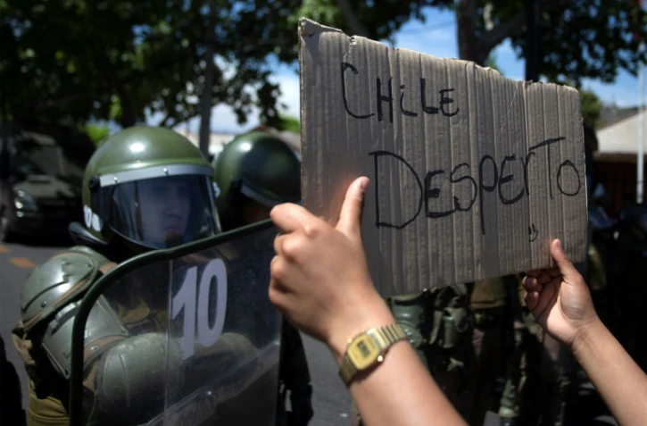 Un manifestant brandit une pancarte proclamant "le Chili s'est réveillé" devant les forces de l'ordre, au cinquième jour d'une violente contestation sociale, le 22 octobre 2019 à Santiago
