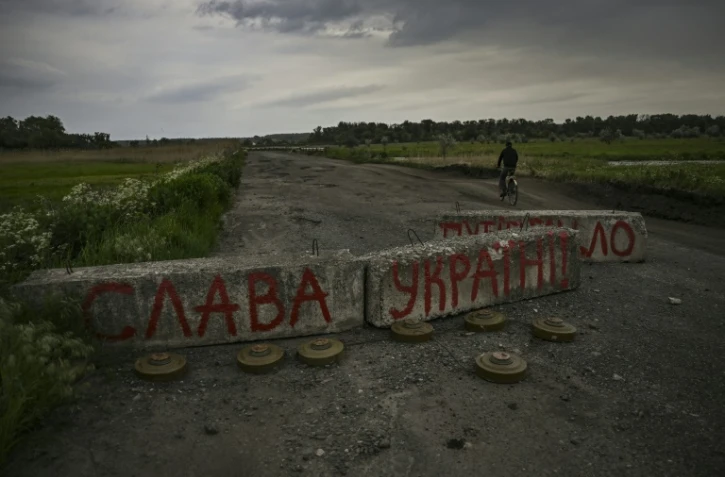 Un civil passe en vélo un barrage routuer sur lequel est écrit "Gloire à l'Ukraine" près de Barvinkove, dans le Donbass, dans l'est de l'Ukraine, le 29 mai 2022