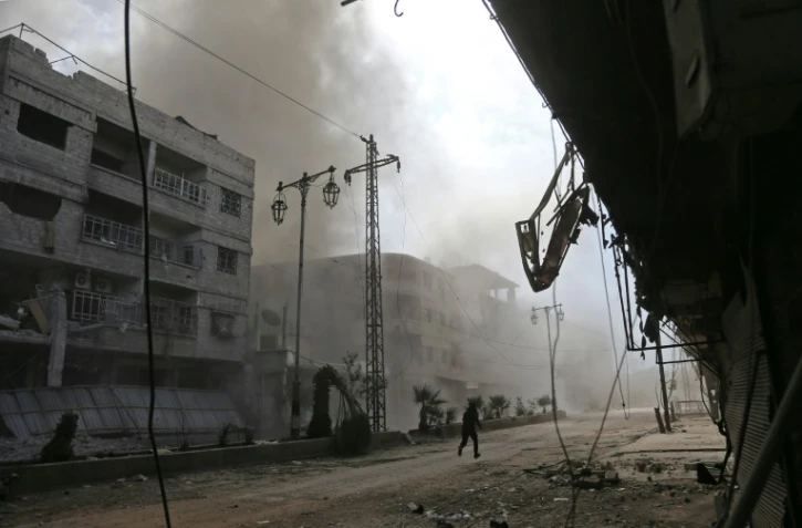 De la fumée et de la poussière s'élèvent d'une rue après des raids aériens du régime syrien sur la localité de Hammourié, dans le fief rebelle de la Ghouta orientale près de Damas, le 21 février 2018