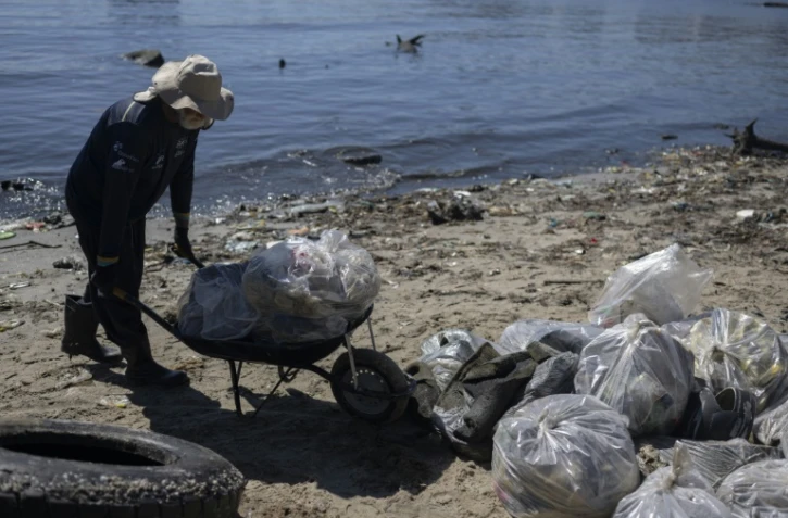 Un homme pousse une brouette pleine de déchets ramassés sur une plage de l'île de Pombeba, dans la baie de Guanabara, le 17 février 2025 à Rio de Janeiro, au Brésil