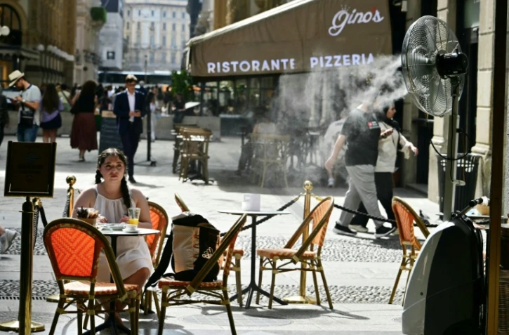 Une jeune fille assise à la terrasse d'un marchand de glaces, sur laquelle un ventilateur-brumisateur a été installé pour se protéger de la chaleur à Milan en Italie, le 27 mai 2026