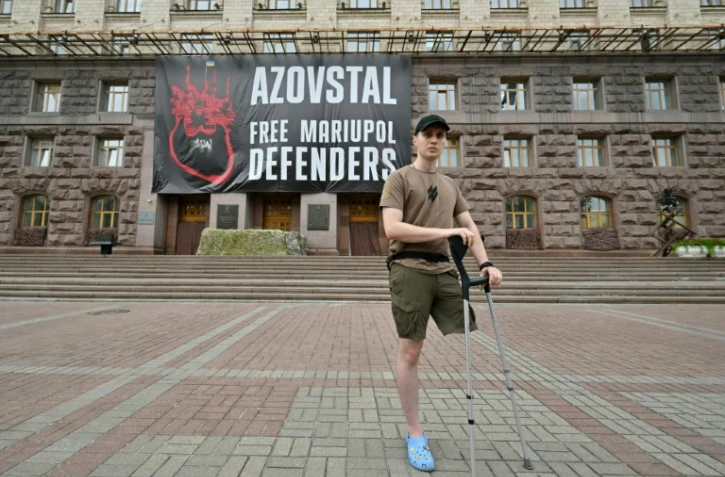 Le soldat ukrainien Vladyslav Jaïvoronok du régiment Azov, amputé d'une jambe, devant une affiche géante "Libérez les défenseurs de Marioupol", le 16 août 2022 à Kiev