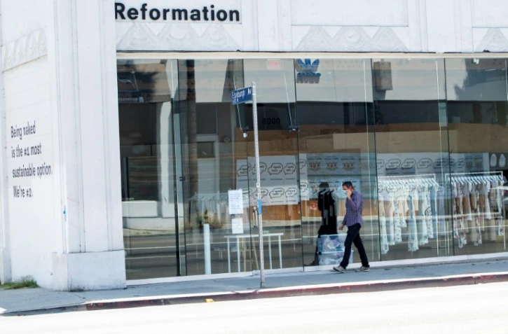 Une personne portant un masque passe devant un magasin fermé sur l'avenue Melrose à Los Angeles, le 3 août 2020