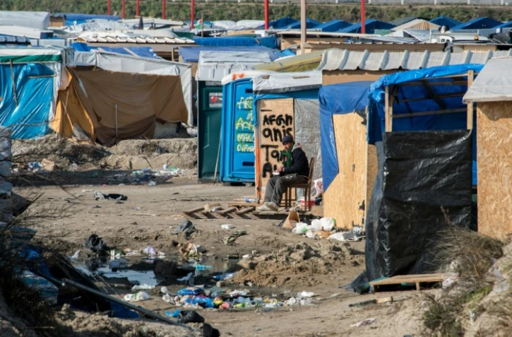 Un homme assis au milieu de cabanes de fortune dans la "Jungle" de Calais, le 16 mars 2016