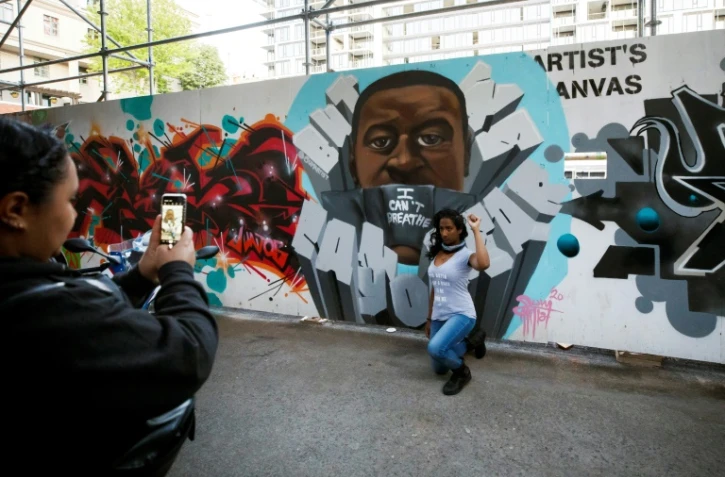 Une femme, genou à terre et poing levé, devant une peinture murale représentant George Floyd, le 11 juin 2020 à Graffiti Alley, à Toronto