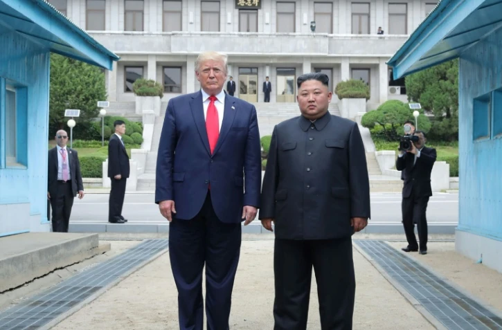 Photo fournie le 1er juillet 2019 par l'agence nord-coréenne Kcna du dirigeant nord-coréen Kim Jong Un (d) et le président américain Donald Trump se tenant au nord de la ligne de démarcation entre les deux Corées, le 30 juin 2019 à Panmunjom