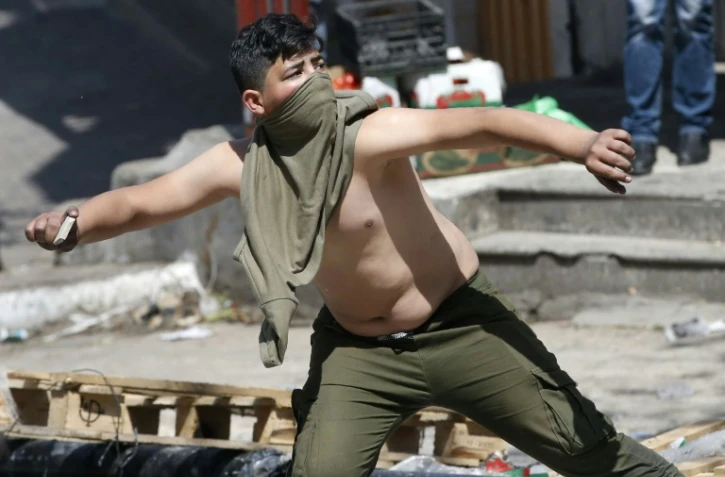 Un manifestant palestinien jette des pierres sur des soldats israéliens le 31 mars 2018 à Hébron, en Cisjordanie