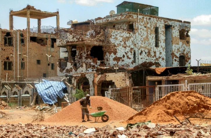 Un ouvrier pellette des cailloux dans une brouette près d'un bâtiment fortement endommagé de la banlieue de Lambab, à la périphérie de Khartoum, le 30 juillet 2025 au Soudan