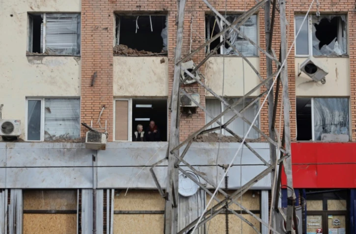 Des habitants regardent à travers la fenêtre d'un bâtiment endommagé après un bombardement à Mykolaïv, le 19 avril 2022