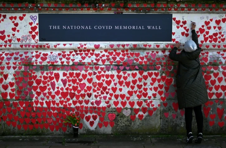 Une femme écrit sur le mur commémoratif national dédié aux victimes du Covid, le 3 mars 2024 à Londres