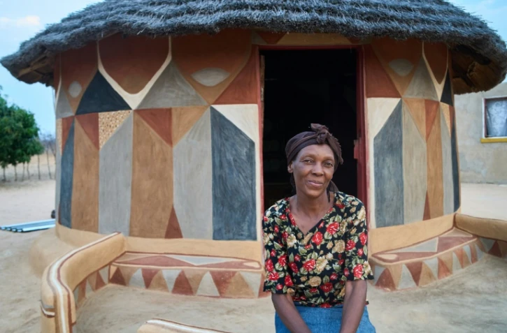 L'artiste Peggy Masuku devant une maison peinte à Matobo, le 29 septembre 2024 au Zimbabwe