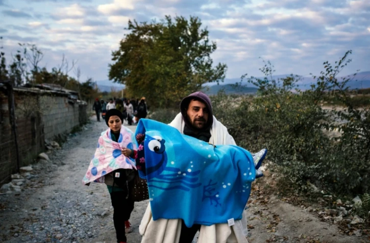 Un homme porte son enfant alors qu'il vient avec d'autres migrants de passer la frontière gréco-macédonienne près de Gevgelija, en Macédoine, le 15 novembre 2015
