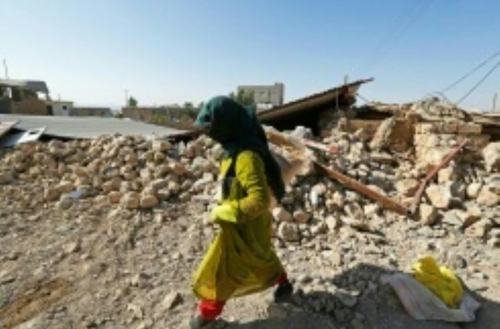 Photo prise le 15 novembre 2017 à Kouik (nord-ouest de l'Iran) montrant une femme marchant dans les décombres d'un bâtiment détruit par le séisme du 12 novembre 