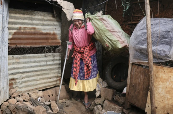 Molly Aluoch s'appuie sur une béquille pour porter un sac de déchets plastiques usagés collectés dans le bidonville de Kibera, à Nairobi, le 11 août 2025 au Kenya