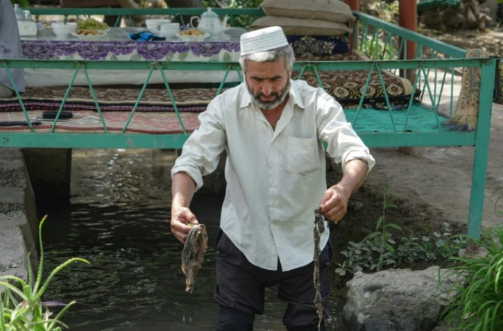 Nematoullo Bassirov, 58 ans, montre des déchets ramassés dans le canal d'irrigation qui passe dans sa cour, le 27 août 2025 à Kolkhozobod, dans le sud-ouest du Tadjikistan