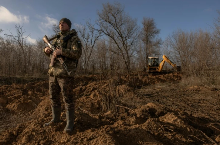 Un soldat ukrainien surveille le ciel en cas d'attaque de drones pendant qu'une tractopelle creuse des tranchées dans la région de Zaporijjia, le 30 janvier 2024