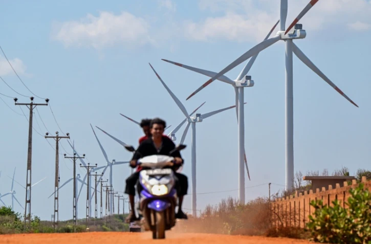 Cette photo, prise le 2 octobre 2026, montre un motard passant devant des éoliennes installées le long d'une route de la péninsule de Mannar, au Sri Lanka