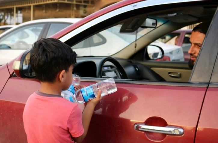 Un garçon irakien essaye de vendre des bouteilles d'eau dans une rue de Mossoul, où des enfants orphelins errent pour mendier ou vendre des objets futiles pour survivre, un an après la reprise par l'armée irakienne de la ville aux jihadistes, le 7 juillet 2018