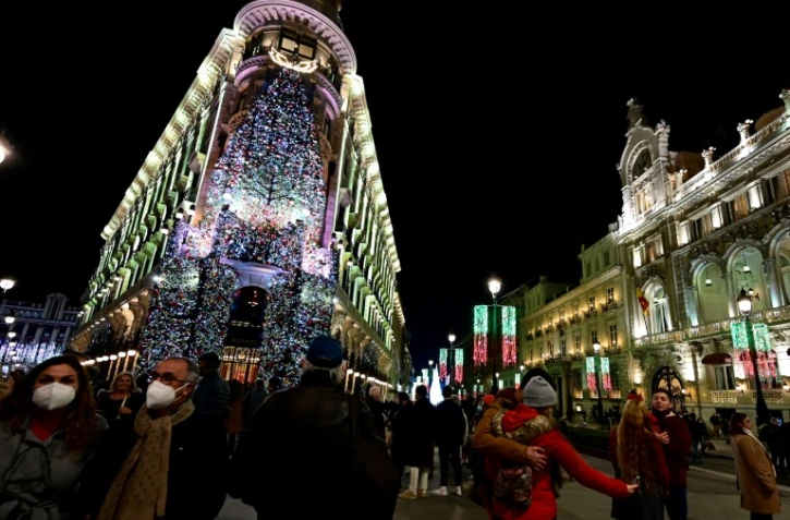 Des passants déambulent masqués dans les rues illuminées de Madrid, le 22 décembre 2021 au lendemain de l'annonce du retour du masque obligatoire à l'extérieur en Espagne