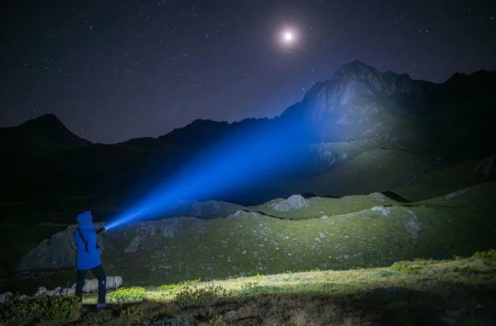 Aliki Buhayer-Mach, bénévole de l'ONG Oppal pour la protection des alpages, utilise une puissante torche pour éclairer une montagne voisine et voir si des loups sont présents, le 10 août 2023 à Pontimia, dans les Alpes suisses 
