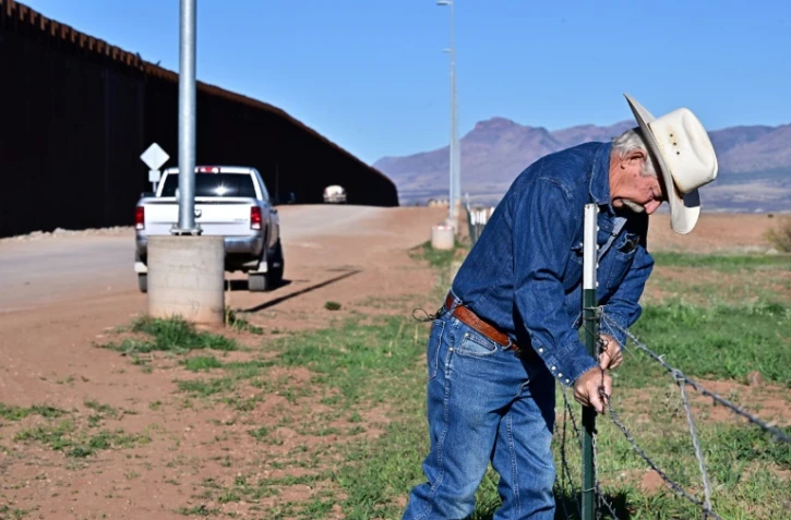 L'éleveur John Ladd ajuste la clôture endommagée délimitant ses terres, le long du mur à la frontière entre les Etats-Unis et le Mexique, le 17 avril 2024 près de Palominas, en Arizona
