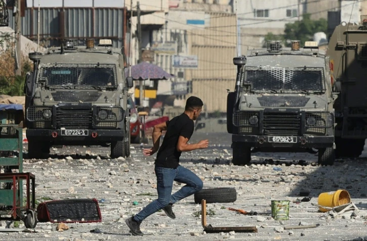 Un Palestinien court devant des véhicules militaires israéliens stationnés dans la vieille ville de Naplouse en Cisjordanie occupée, le 9 août 2022     
