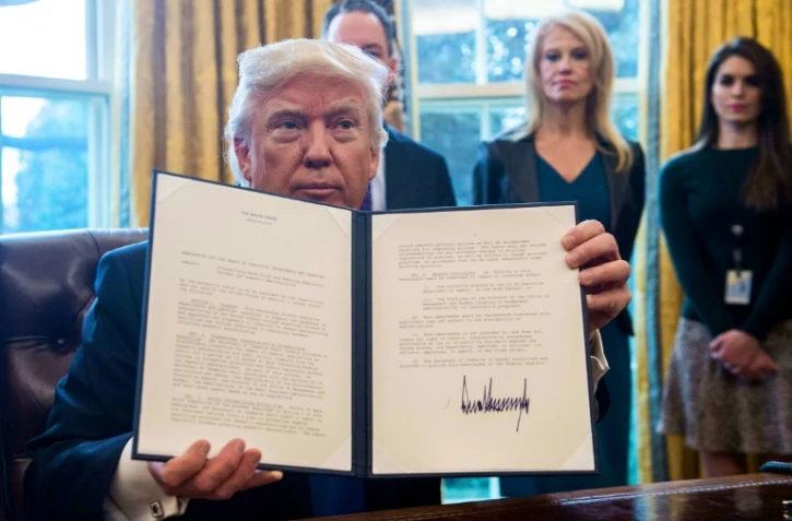Le président Donald Trump montre l'un des décrets qu'il vient de signer, le 24 janvier 2017 dans le Bureau Ovale de la Maison Blanche, à Washington