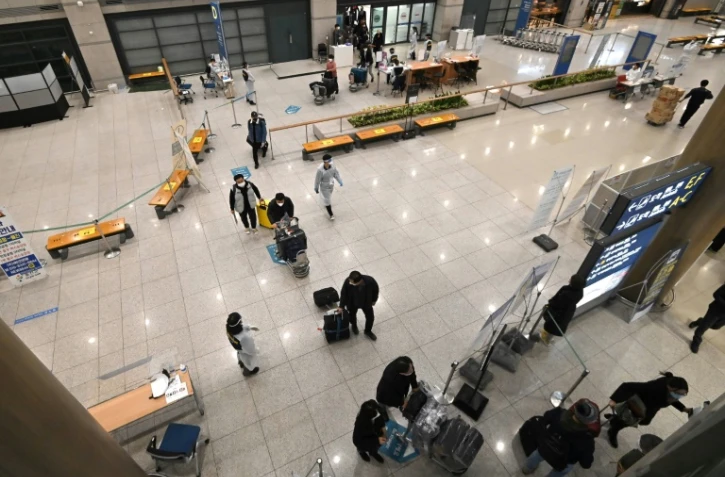 Des employés en tenue de protection guident les voyageurs le 30 novembre 2021 dans le hall des arrivées de l'aéroport international d'Incheon, en Corée du Sud