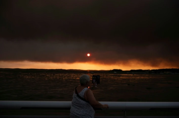 Une femme observe la fumée depuis la plage à Andernos-les-Bains lors d'un incendie dans la forêt de Lège-Cap-Ferret, dans le sud-ouest de la France, le 23 juillet 2026, alors qu'une partie de la zone voisine a été évacuée