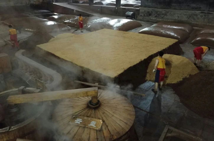 Des employés mélangent une purée de céréales dans des cuves en terre pour la fabrication du baijiu, le 24 avril 2019 dans une distillerie à Luzhou, dans la province chinoise du Sichuan