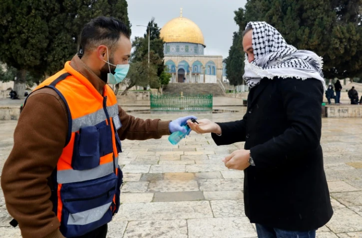 Un volontaire propose du gel hydroalcoolique à un palestinien en route pour la prière du vendredi, devant la mosquée Al-Aqsa à Jérusalem, le 20 mars 2020