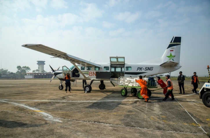 Des agents de l'Agence nationale de gestion des catastrophes chargent du chlorure de sodium dans un avion avant une opération d'ensemencement des nuages à Palangkaraya, dans le Kalimantan central, le 2 août 2026 en Indonésie